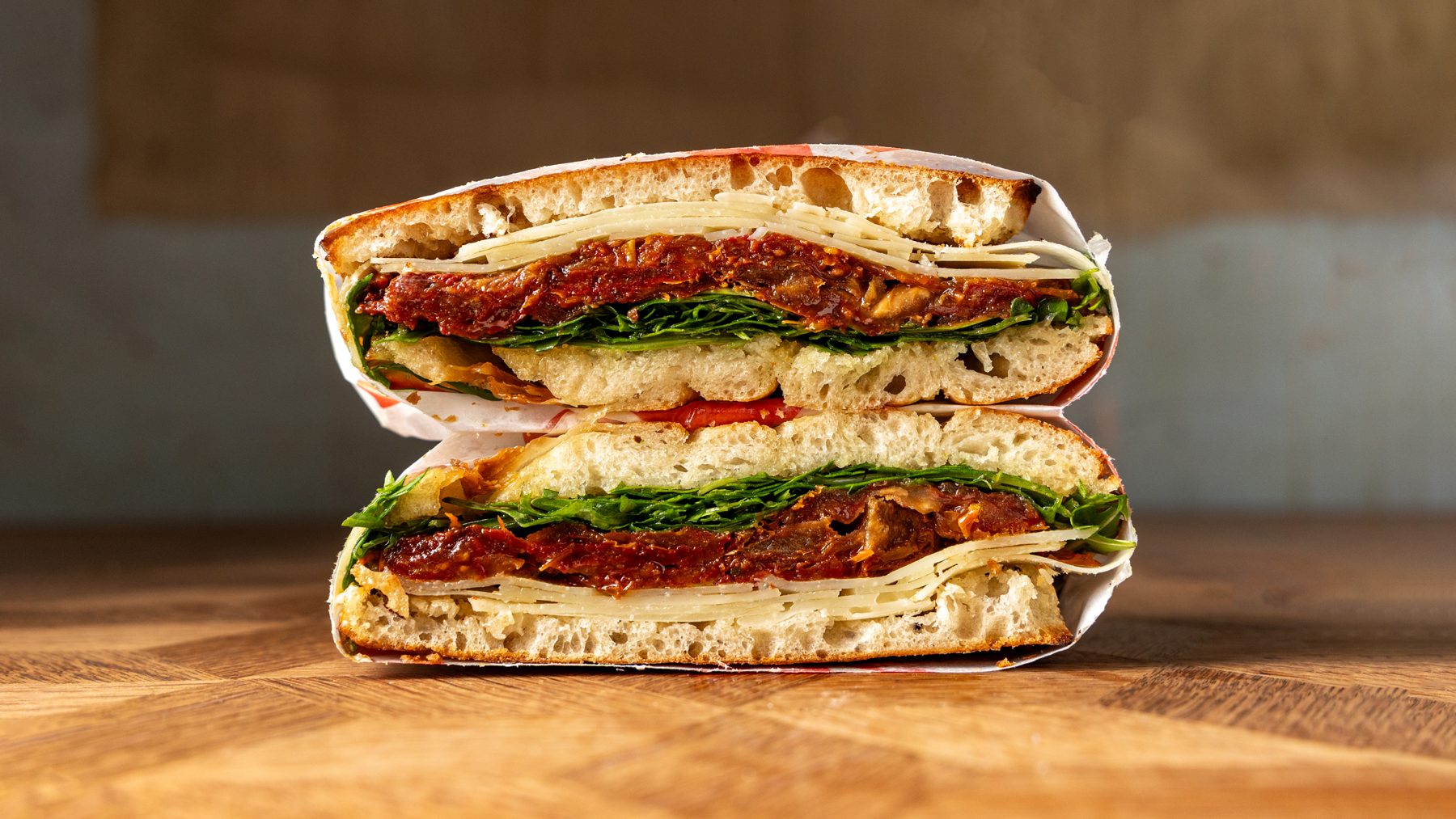 The Basic Bella vegetarian schiacciata cut in half showing asiago, sundried tomatoes, rocket and hot honey on Tuscan bread