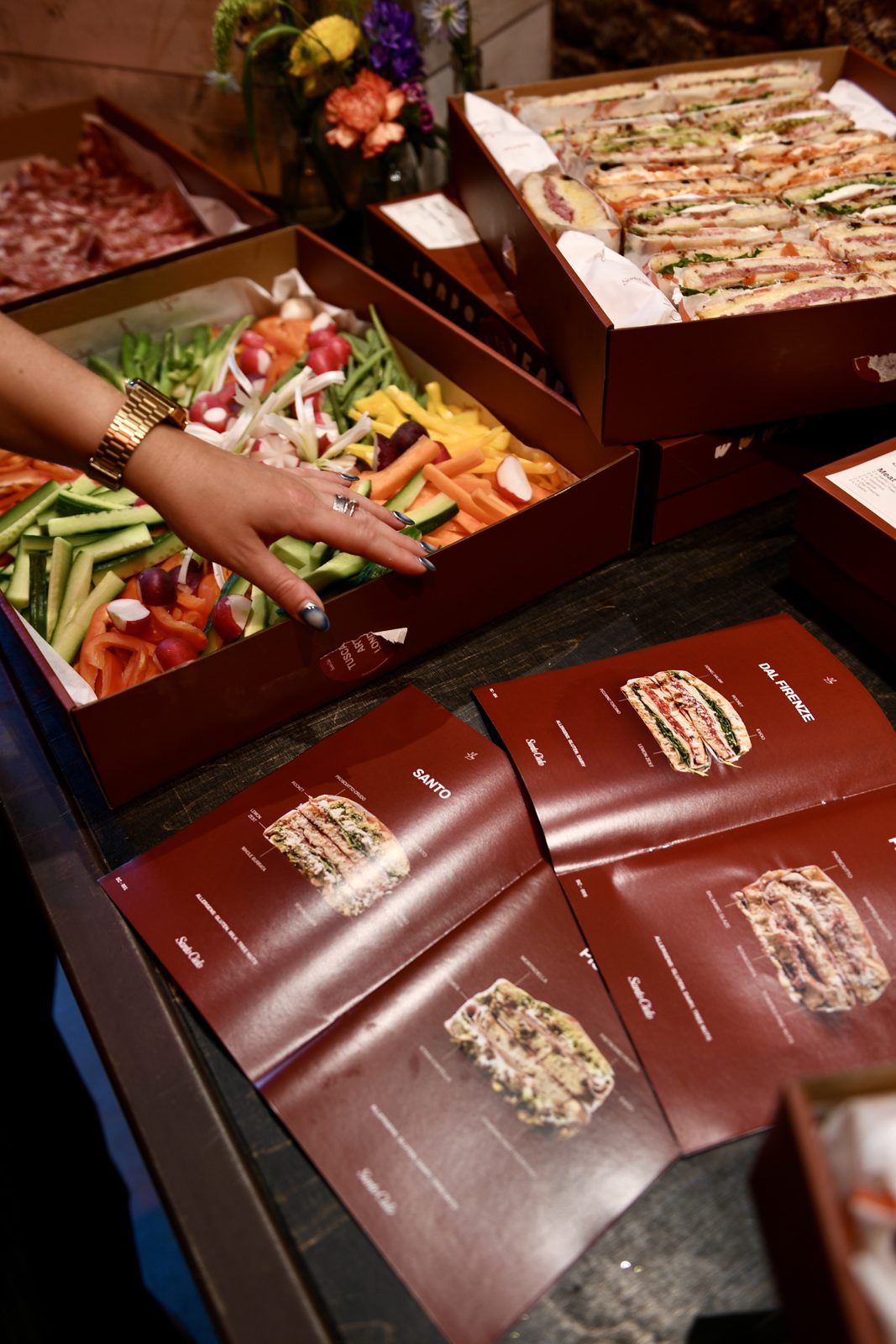 Guest reaching over a colourful crudites box beside Santo Cielo menu cards at the Bio and Me event