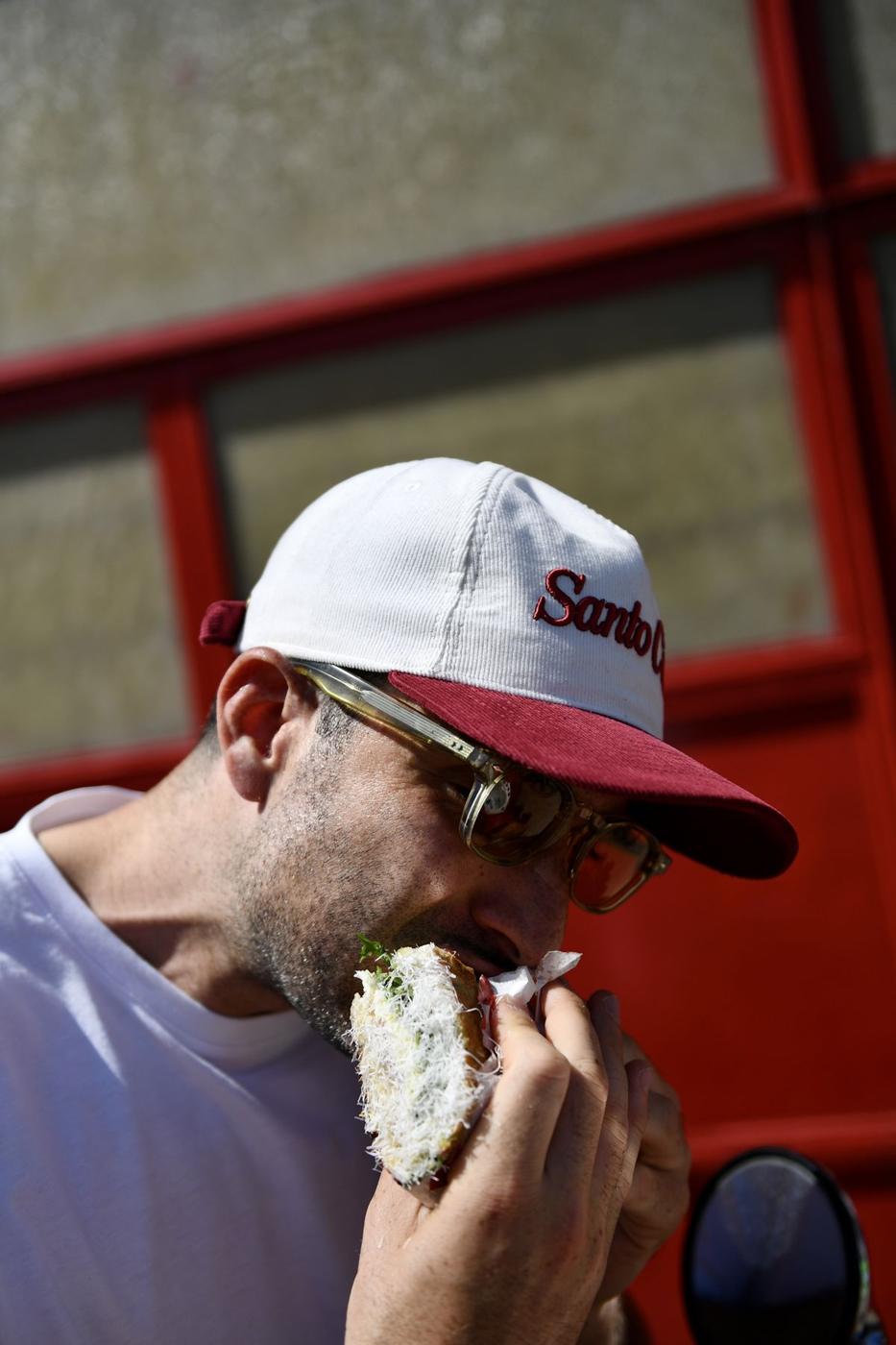 Someone in the SC Summer Hat taking a bite of a schiacciata against the red shop front