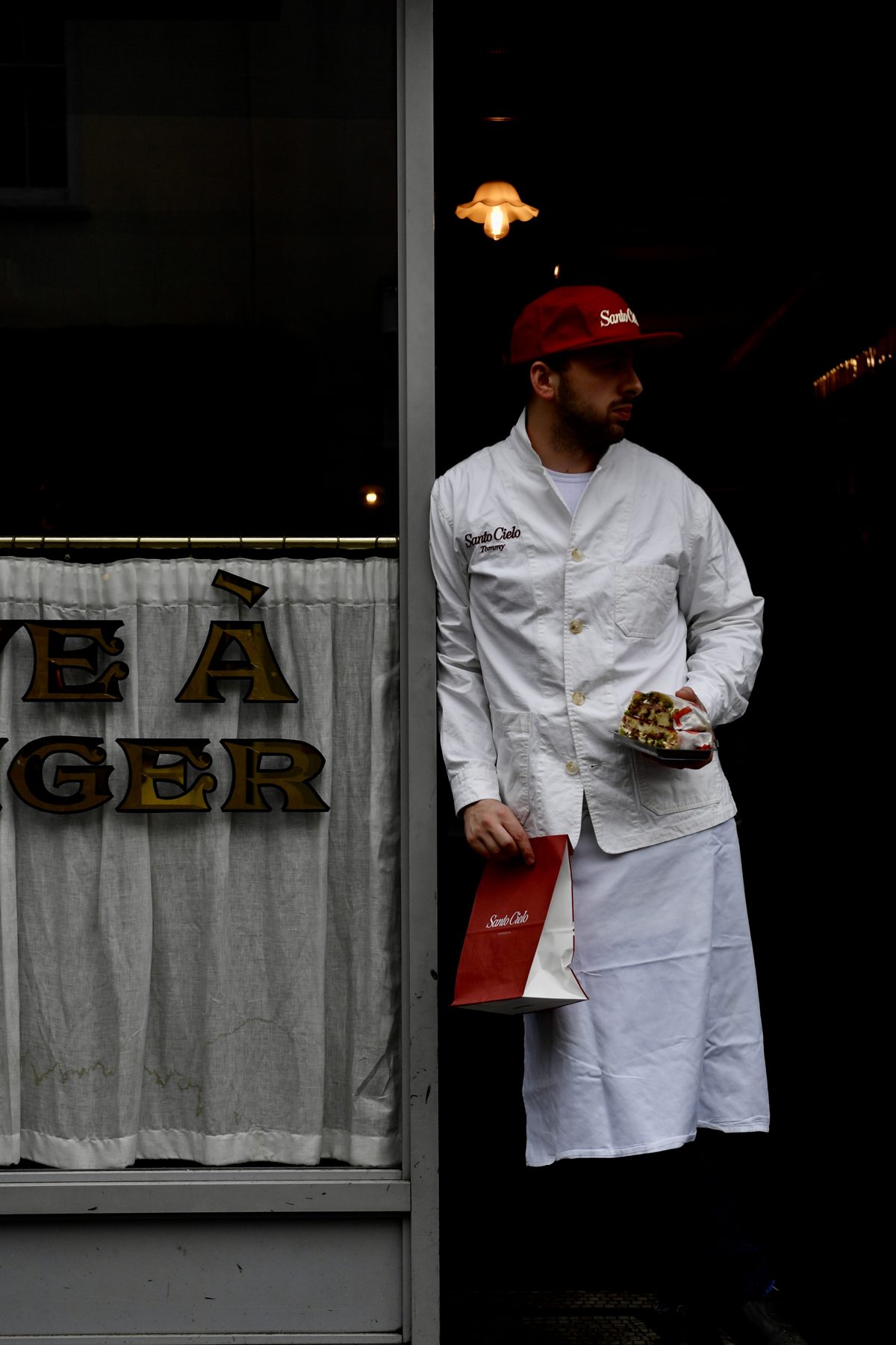 Santo Cielo team member in the shop doorway with a sandwich and a red takeaway bag