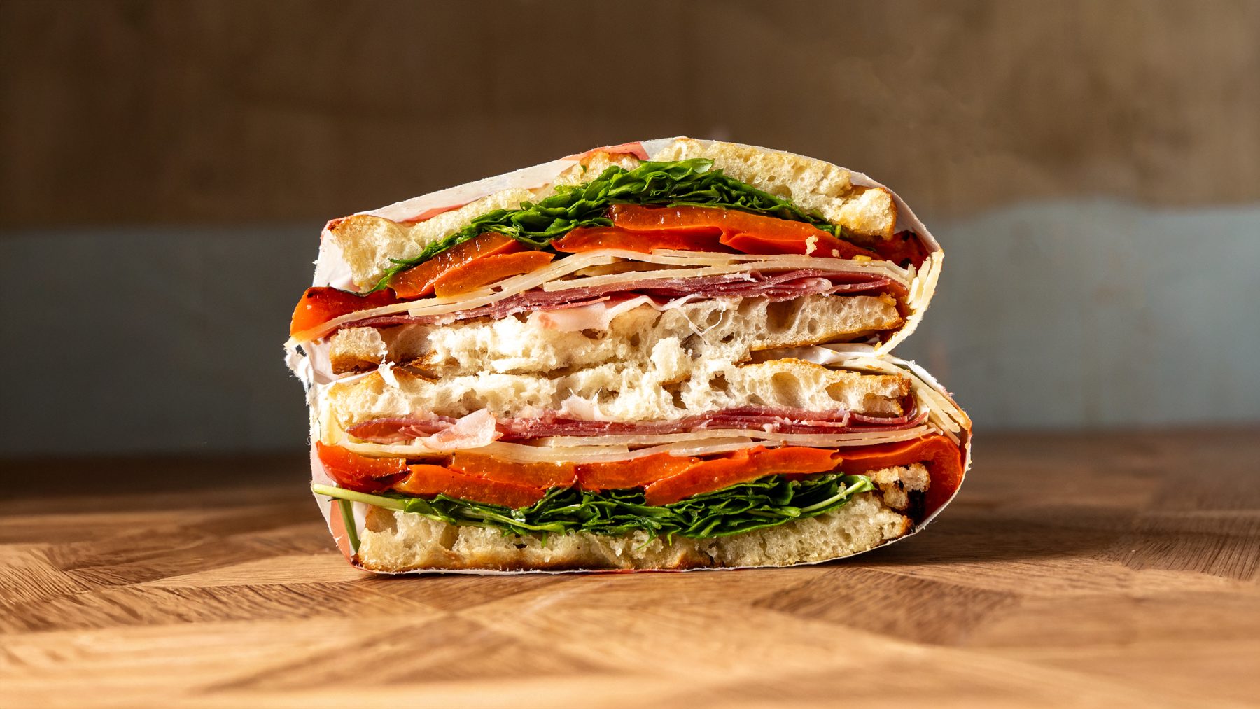 The Il Napoli schiacciata cut in half showing Napoli salami, provolone, roasted red peppers and rocket on Tuscan bread