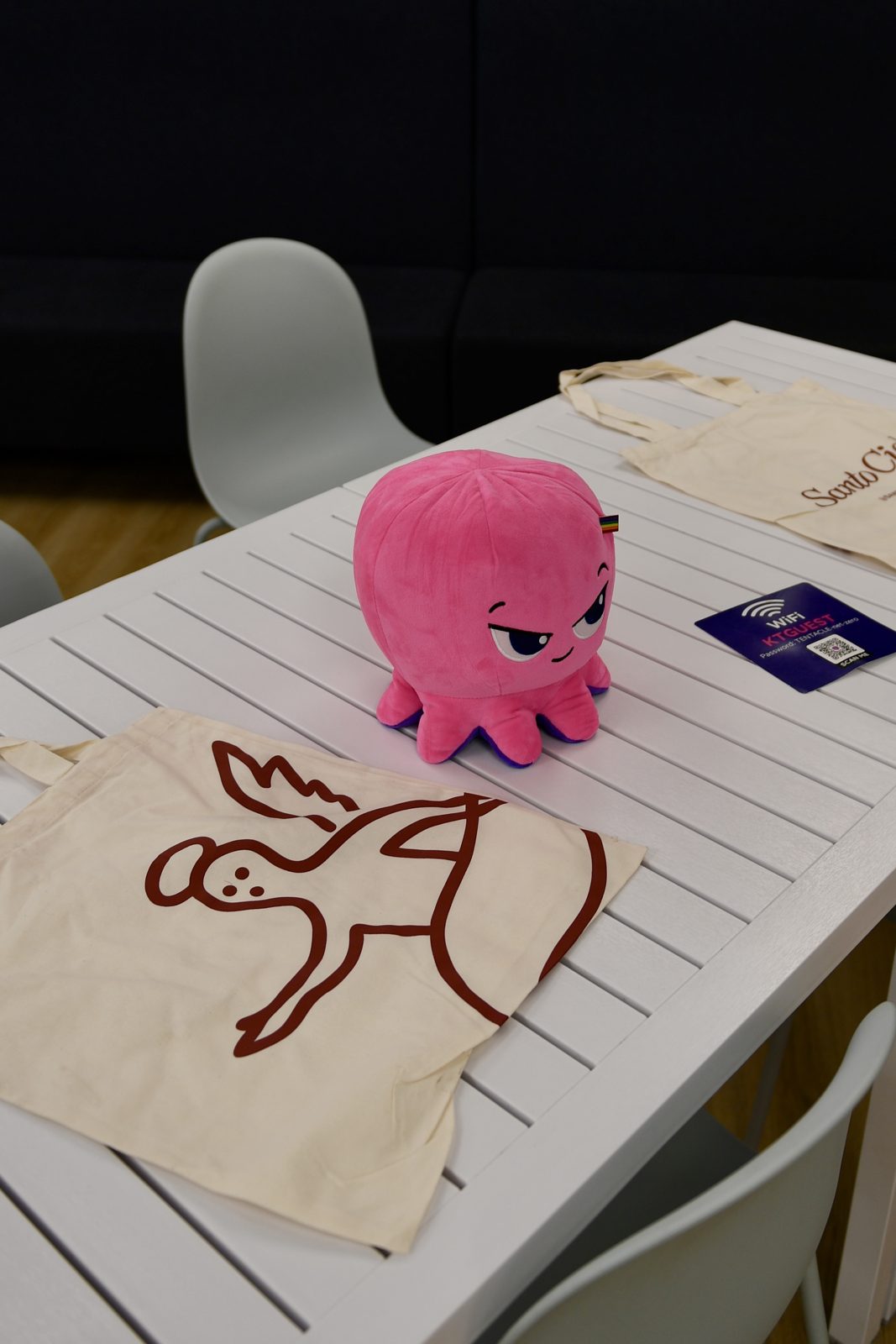 Kraken octopus plush next to Santo Cielo angel tote bags on a table at the pop up