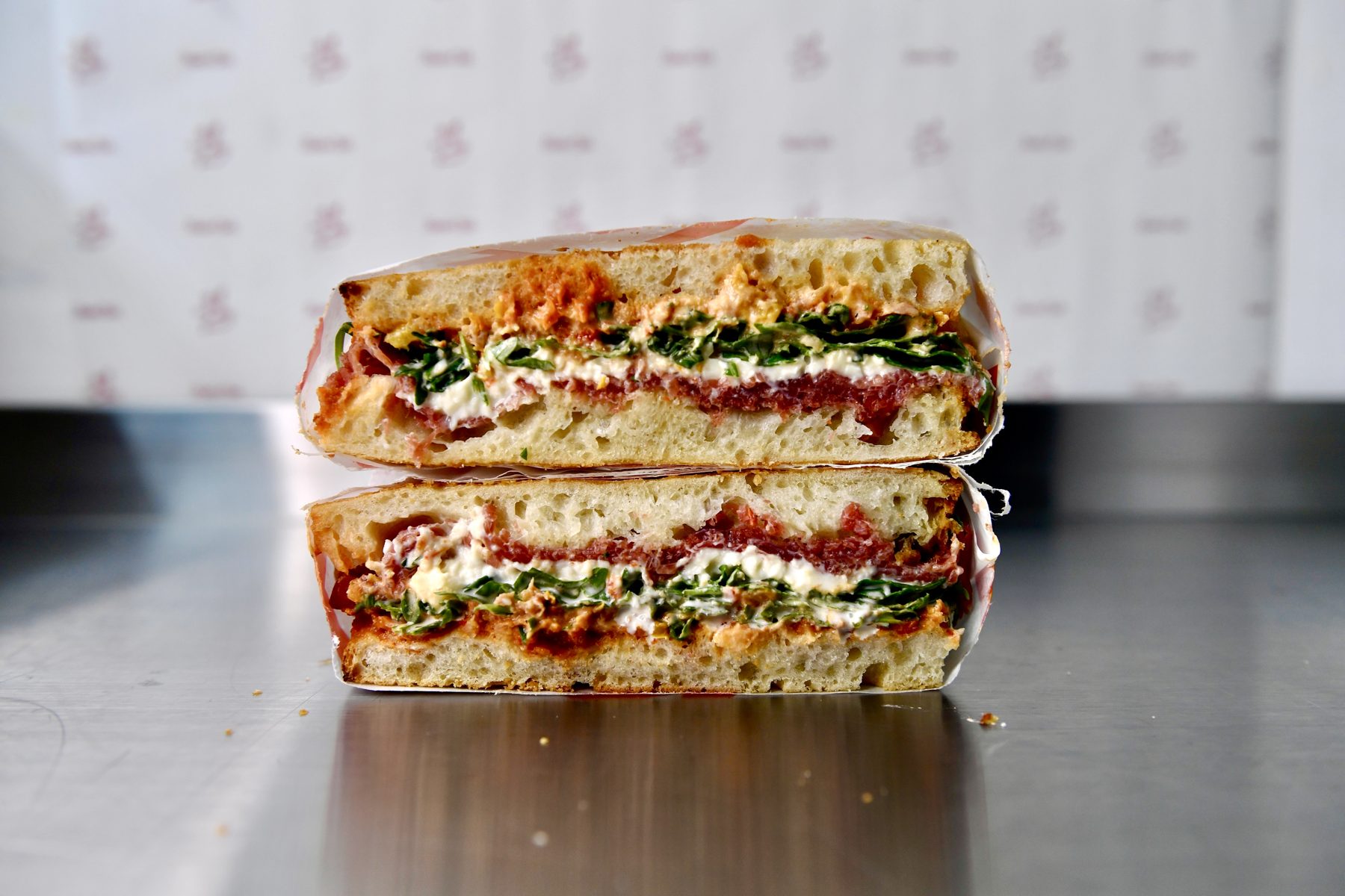 The Manzo Special schiacciata cut in half showing bresaola, stracciatella, nut free romesco and rocket on Tuscan bread