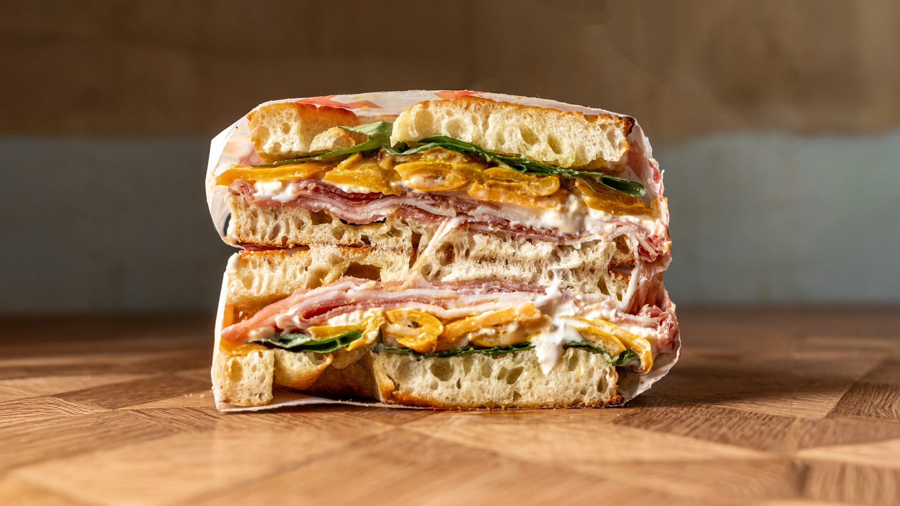 The Miso Rossetto schiacciata cut in half showing speck, stracciatella, yellow peppers and miso honey crema on Tuscan bread