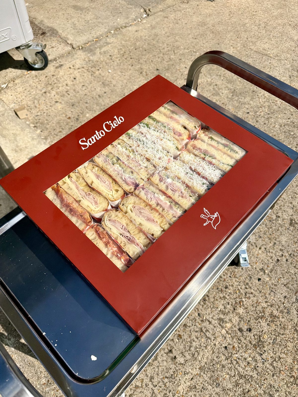 Red Santo Cielo platter box with a window showing rows of mixed schiacciata sandwiches on a delivery trolley