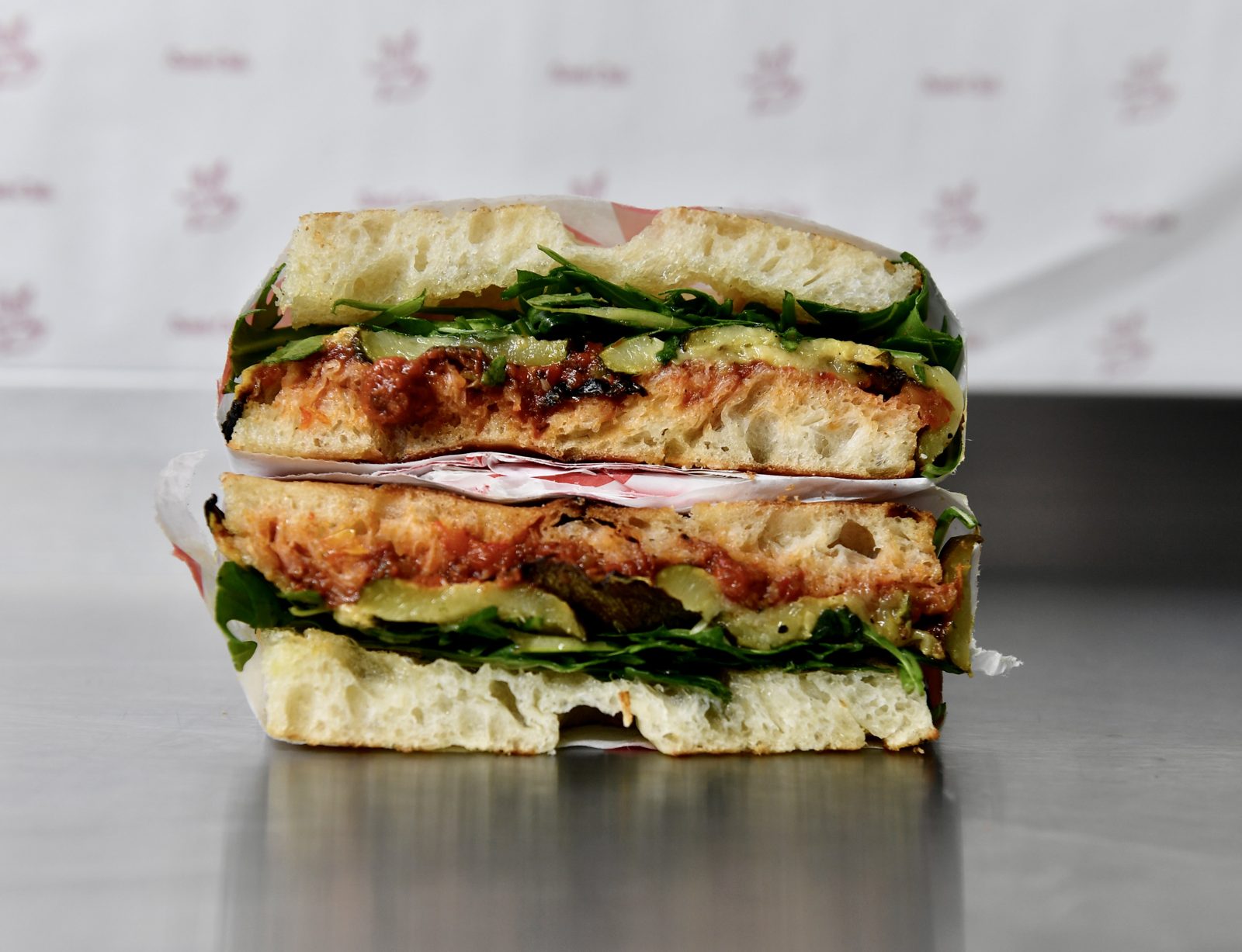 The Phoebe Fresca vegan schiacciata cut in half showing nut free romesco, charred courgettes, truffle agave, rocket and lemon zest on Tuscan bread