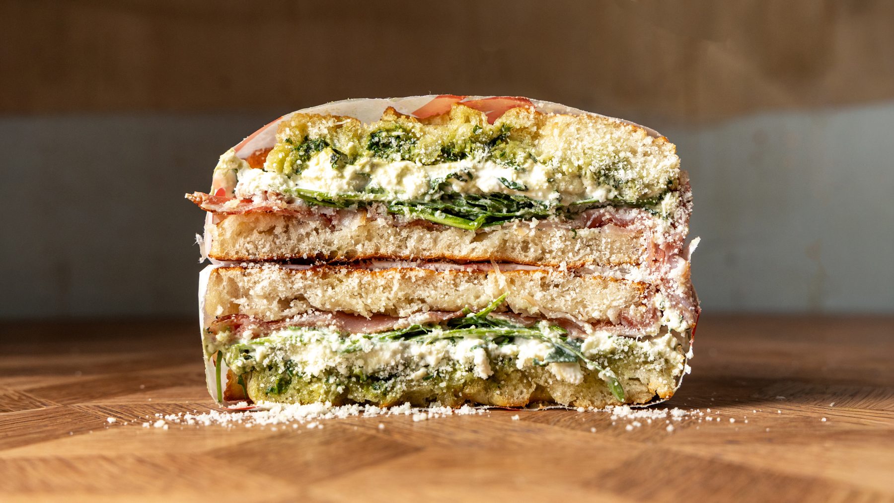 The Santo Special schiacciata cut in half showing prosciutto crudo, burrata, basil pesto, rocket and pecorino on Tuscan bread