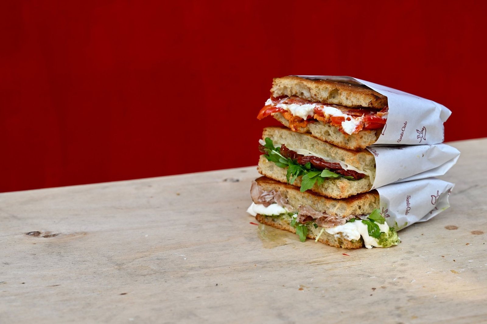 Three schiacciata sandwiches in a stack on a wooden table against a red wall