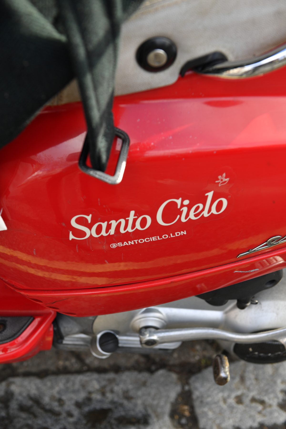Santo Cielo sticker with the @santocielo.ldn handle on the side of the red delivery Vespa