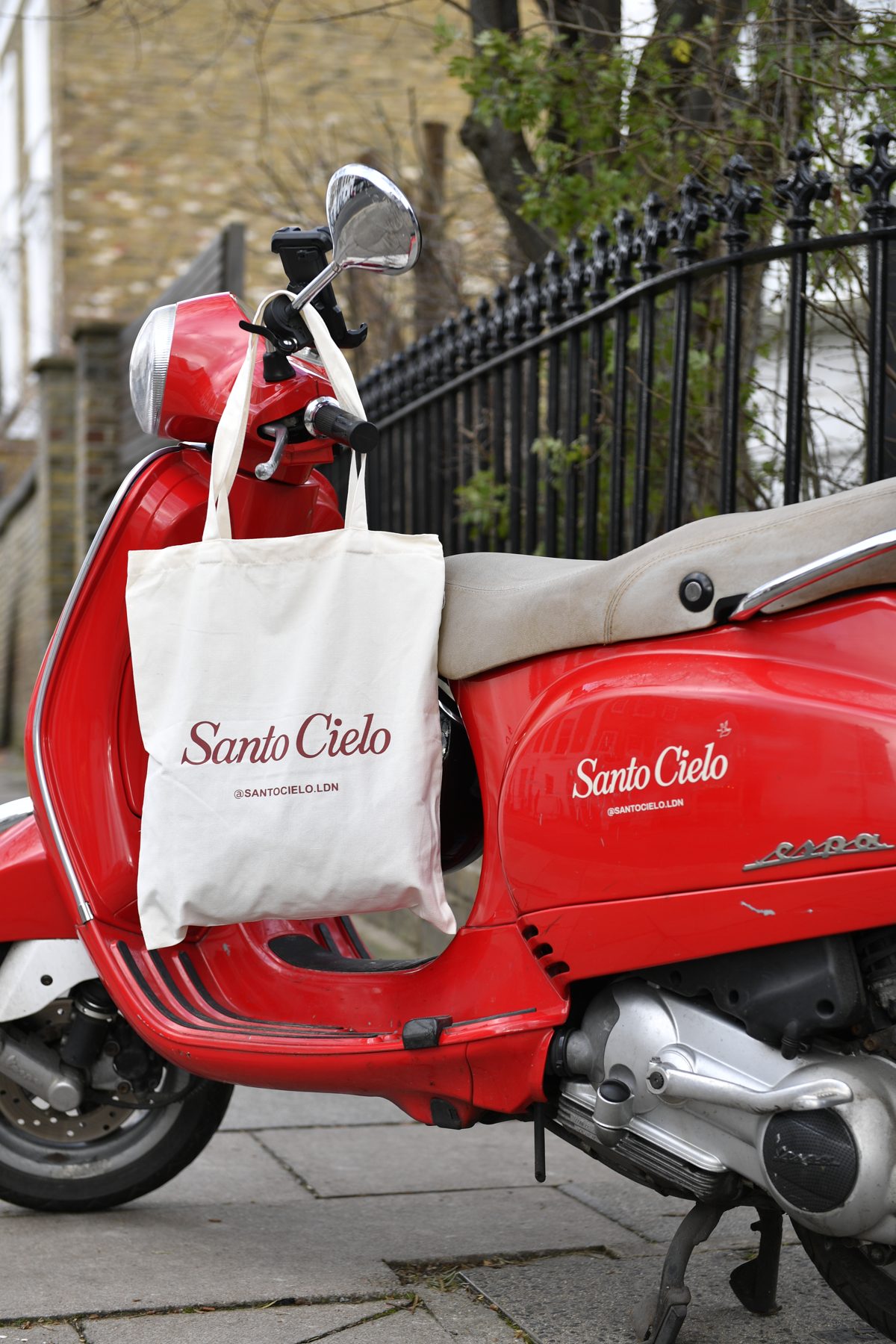 Cream Santo Cielo canvas tote bag hanging from the handlebars of a red Vespa