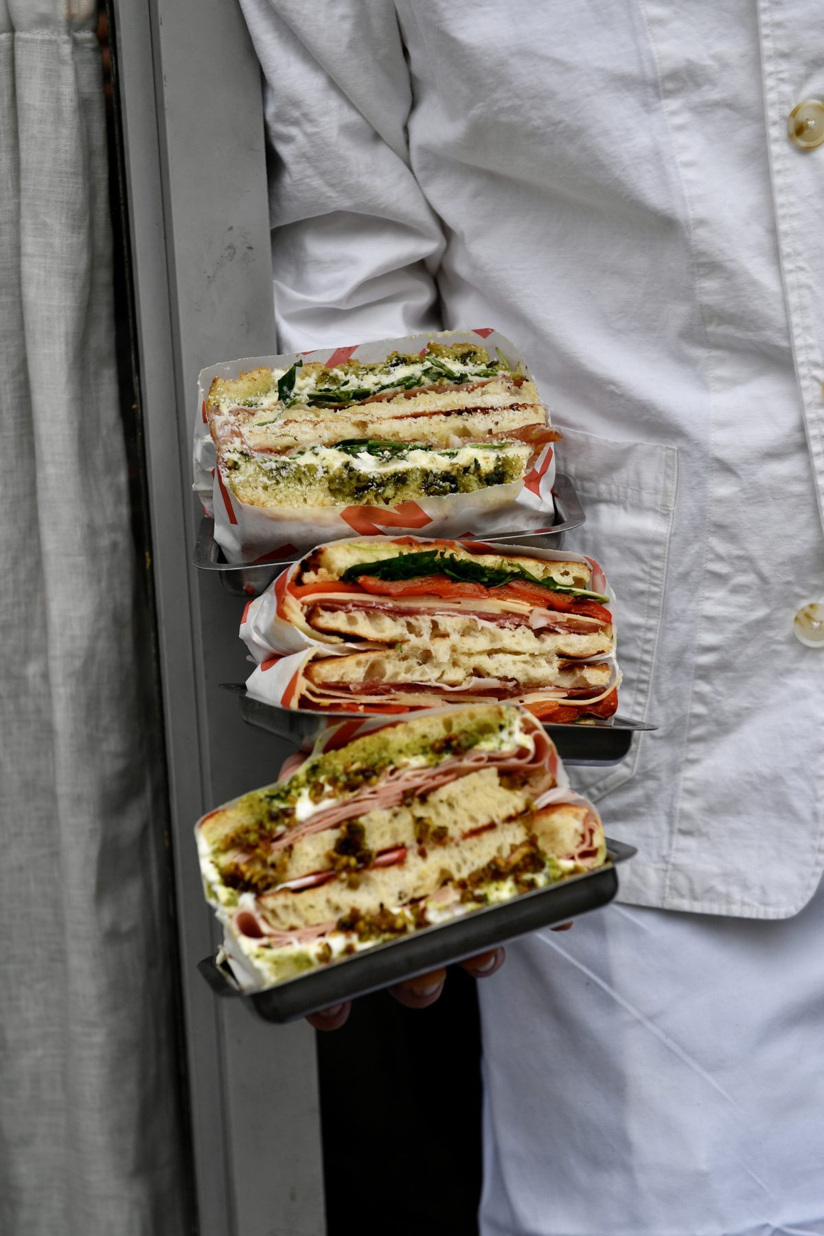 Close up of three individually wrapped schiacciata sandwiches ready for a catering order