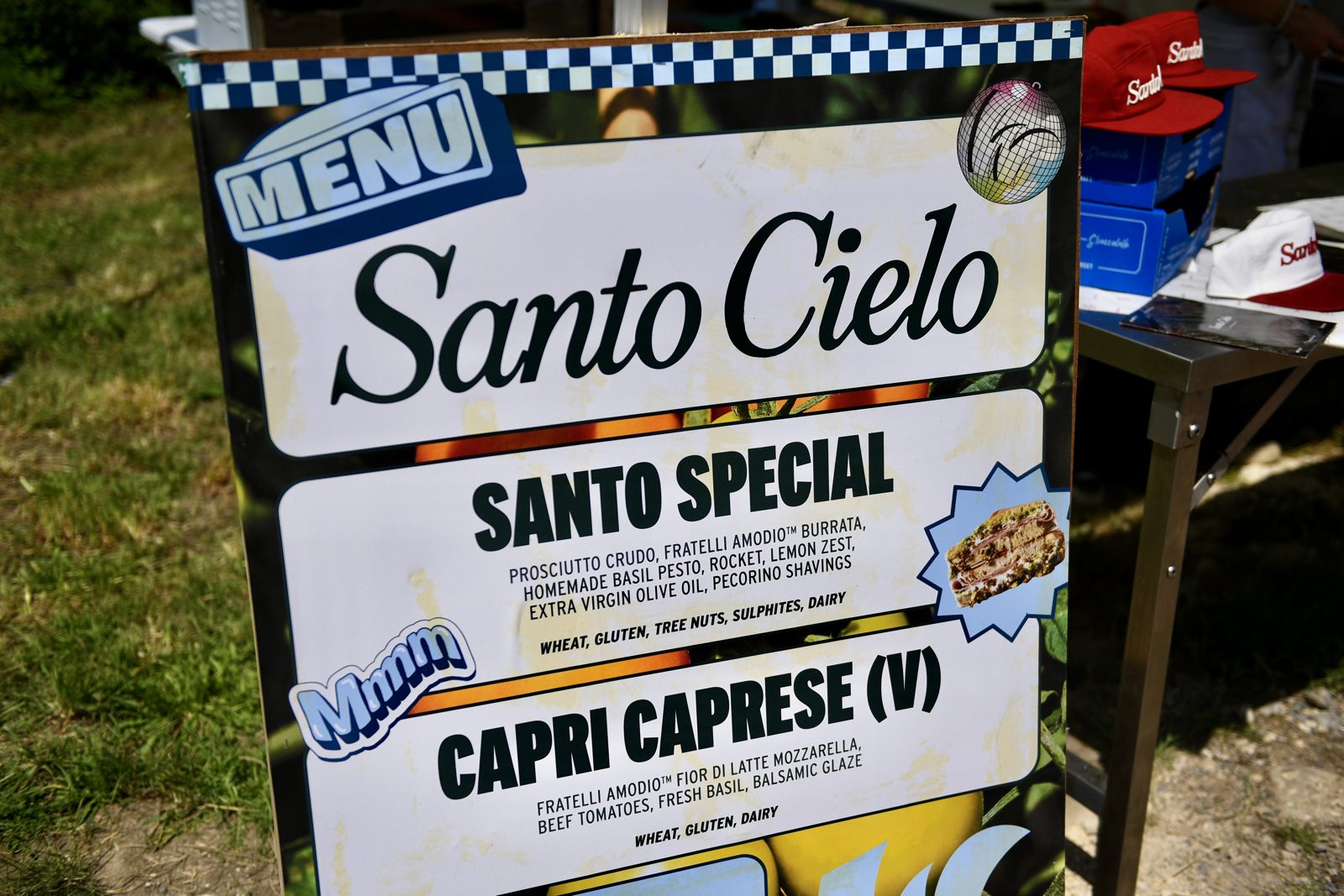 The Santo Cielo festival menu board at Wildfarmed Field Day showing the Santo Special and Capri Caprese, with red caps on the stall